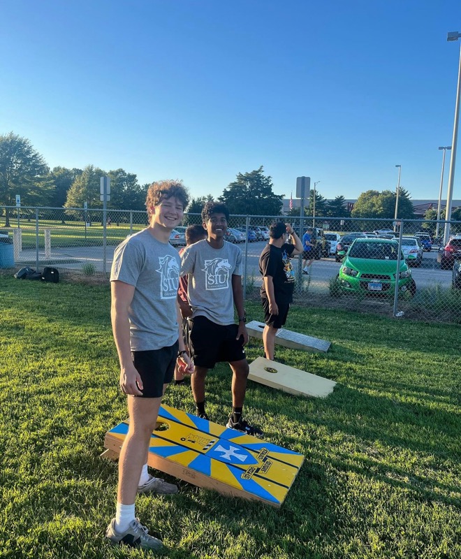 two guys smiling while playing cornhole
